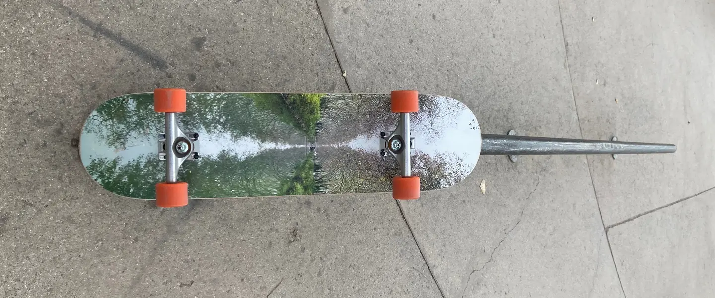 Tabla de skate con una foto impresa, montada con ejes y ruedas, tumbada en el suelo de un skatepark
